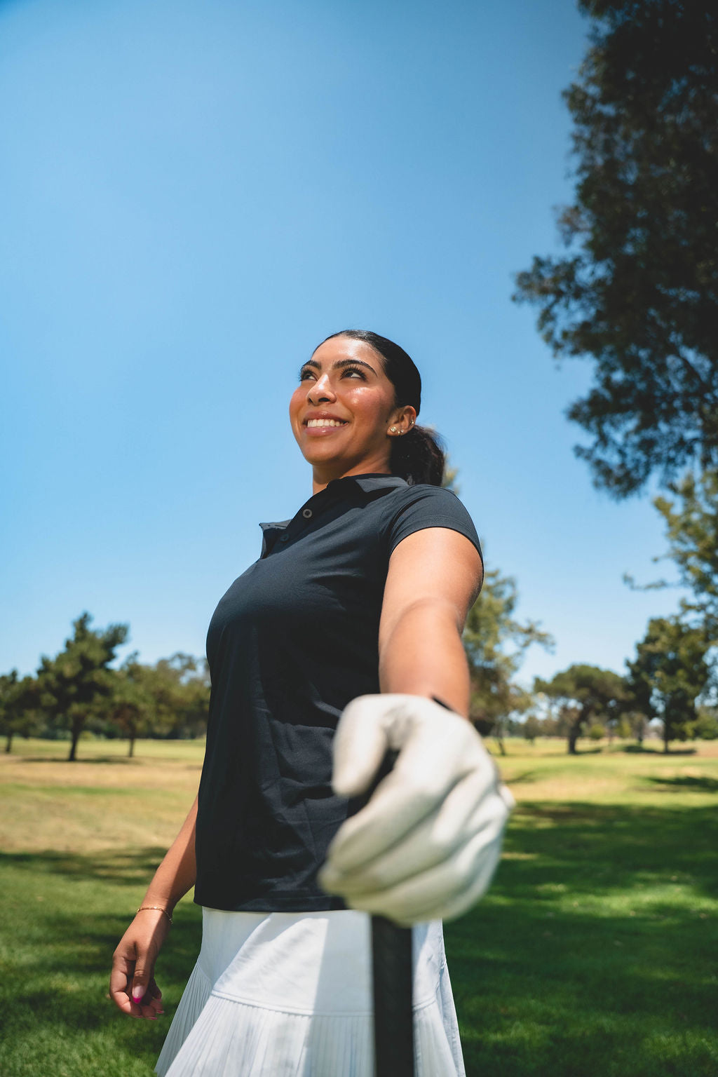 Woman golfer smiling on the course in Kingsmen golf apparel